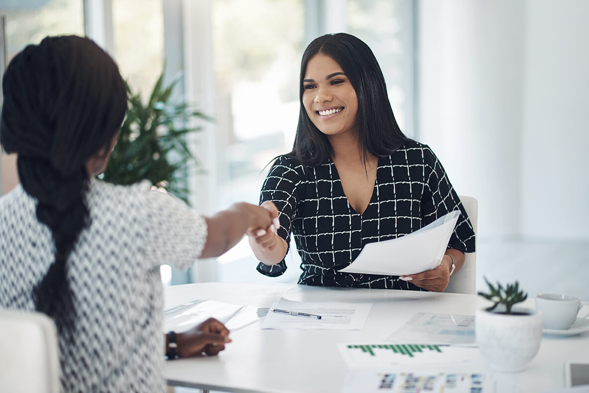 images/insights/2023/female-professional-smiling-while-shaking-hands-sitting-at-a-white-desk.jpg
